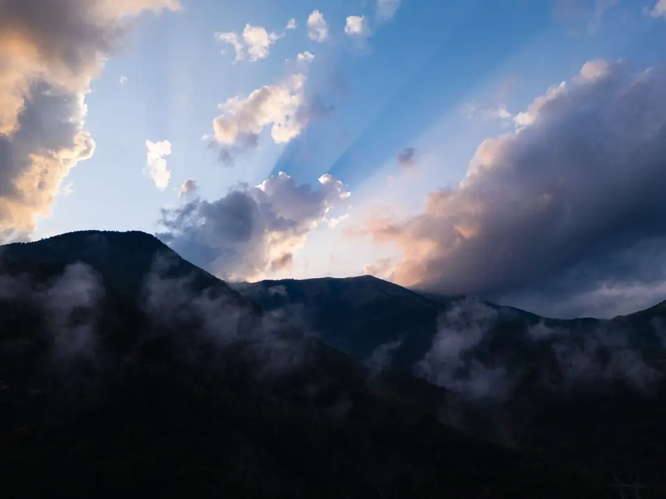 Sunbeams breaking through clouds over misty silhouetted mountains
