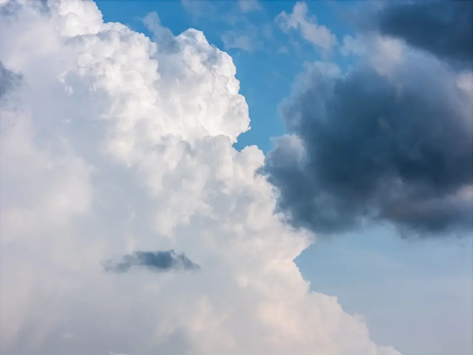 Towering white and dark storm clouds against a blue sky
