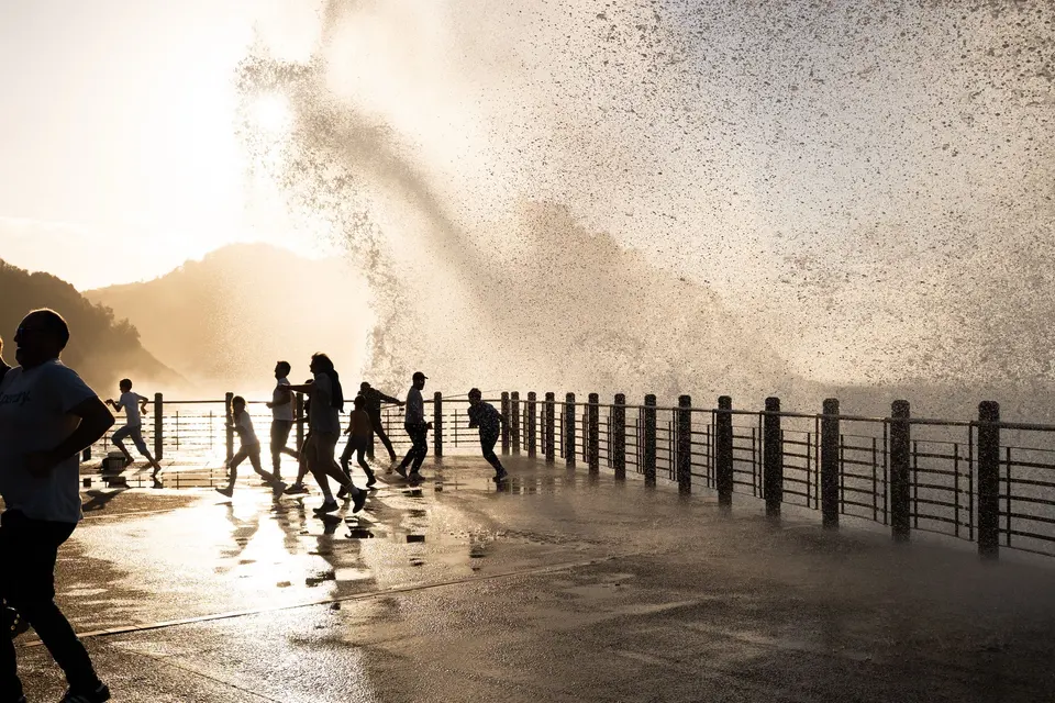 Large wave splashing over a seaside promenade as people run from the spray